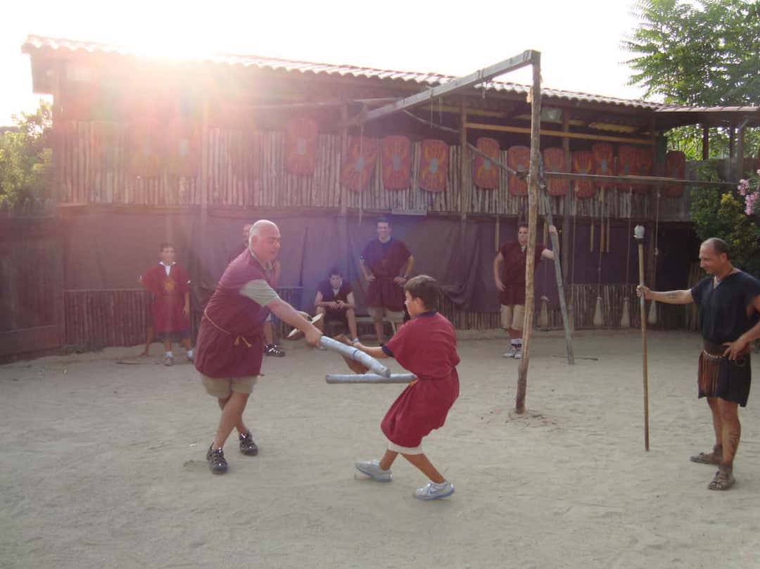 Un homme et un garçon habillés en gladiateurs en train de se battre à l'école des gladiateurs