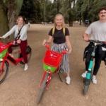 2 filles sur des vélos rouges et verts et un homme sur une trottinette électrique
