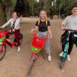 2 filles sur des vélos rouges et verts et un homme sur une trottinette électrique